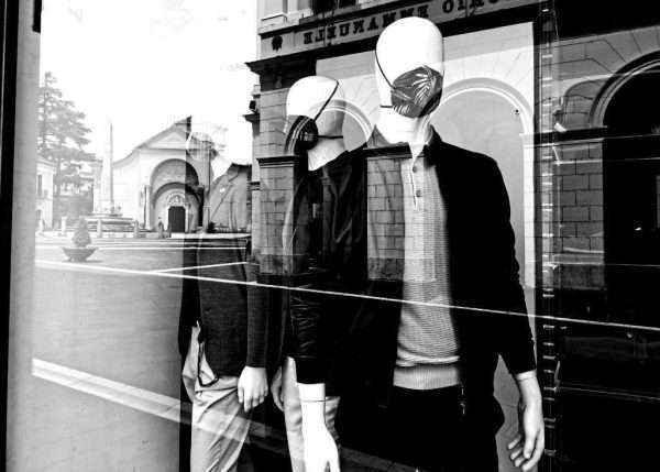 "Corona Fashion" si intitola questa foto in bianco e nero. Si vede la vetrina di un negozio con i manichini che indossano non solo vestiti ma anche le mascherine di design.