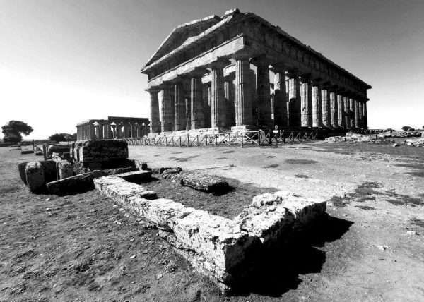 Questa fotografia in bianco e nero è stata scattata a Paestum in Provincia di Salerno. Paestum è conosciuto per il suo parco archeologico molto grande. Gli scavi di Paestum hanno portato alla luce l'intera città di Poseidonia come si chiamava all'era della Magna Grecia. In primo piano si vede il tempio di Nettuno (ovvero Poseidone).