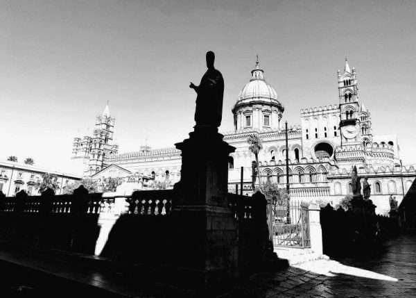 "Im Schatten der Heiligen" significa "All'ombra dei Santi" ma in realtà sono i santi che sono all'ombra. Una fotografia della Cattedrale di Palermo con la statua di papa San Gregorio Magno ovvero Il Grande all'ombra davanti alla basilica.