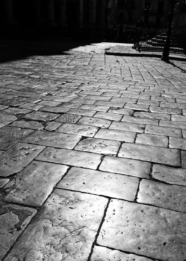 Una fotografia insolita di Palermo con il pavimento di pietre grandi nel centro storico di Palermo. Le pietre ormai lucidate dalle persone che ci camminano riflettono il sole caldo della Sicilia. Un'opera letteralmente del genere Street Photography.